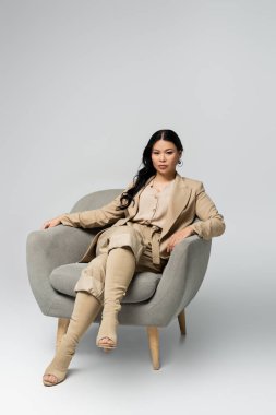 Tam boy Asyalı kadın gri koltukta oturuyor.