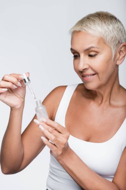 Pipetli serumu gri renkte tutan mutlu yaşlı kadın.