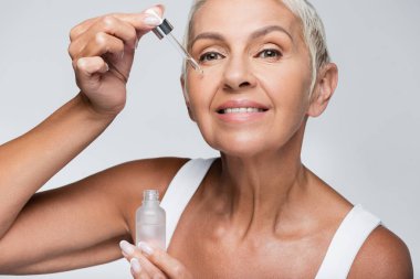 Grey 'e izole edilmiş C vitamini uygulayan mutlu yaşlı kadın.