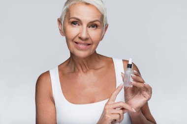 Mutlu yaşlı kadın elinde C vitamini serumuyla gri şişeyi tutuyor.