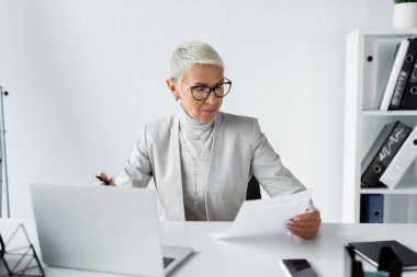 Gözlüklü üst düzey işkadını ofiste belgeye bakıyor. 