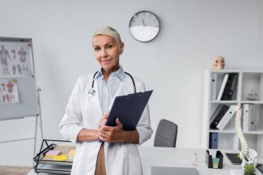 Beyaz önlüklü doktor klinikte pano tutuyor. 