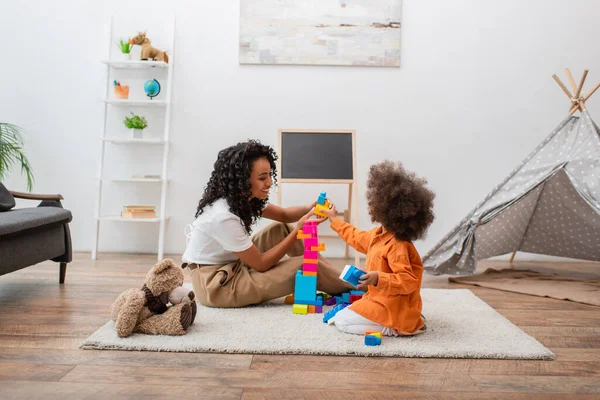 Glimlachende Afrikaanse Amerikaanse Moeder Spelen Bouwstenen Met Kind Buurt Teddy — Stockfoto