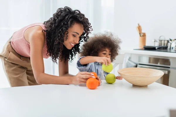 Sonriente Madre Afroamericana Sosteniendo Frutas Cerca Del Niño Cocina — Foto de Stock