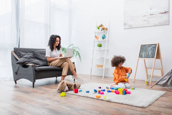 Mujer Sonriente Usando Portátil Sofá Mientras Hija Juega Bloques Construcción — Foto de Stock