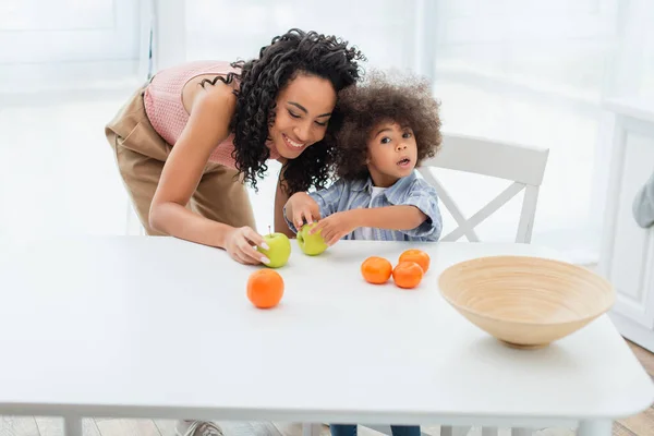 Afro Americano Niño Sosteniendo Manzana Cerca Sonriente Madre Cocina — Foto de Stock