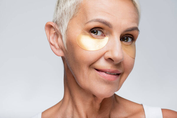 smiling senior woman with collagen eye patches isolated on grey 