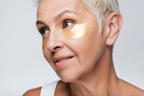senior woman with collagen eye patches looking away isolated on grey 
