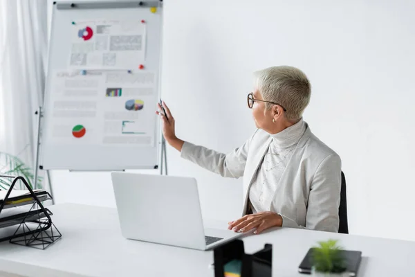 Senior Businesswoman Glasses Pointing Blurred Flip Chart Video Call Laptop — Stock Photo, Image