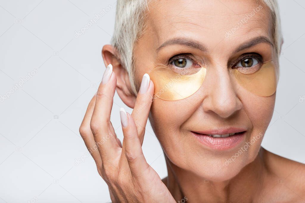 happy senior woman smiling while applying eye patches isolated on grey