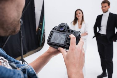 Profesyonel fotoğrafçı fotoğraf stüdyosundaki bulanık modellerin yakınındaki dijital kameraya bakıyor.
