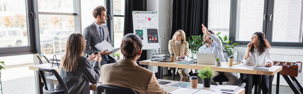 young businessman raising hand during meeting with multiethnic colleagues, banner