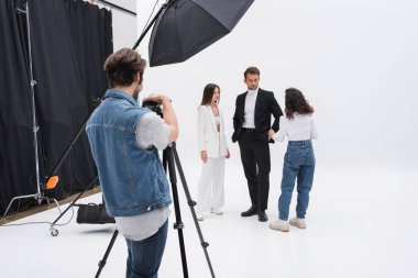 Resim yönetmeni fotoğraf stüdyosunda modellerle konuşurken fotoğrafçı dijital kamerayı ayarlıyor.