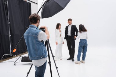 photographer adjusting digital camera while art director talking with models in photo studio clipart