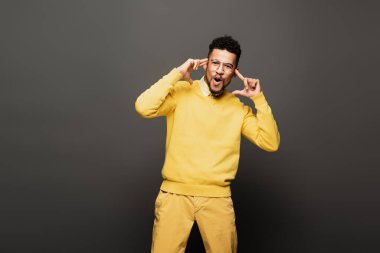 shocked african american man in yellow outfit and glasses on dark grey clipart