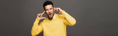 shocked african american man in yellow outfit and glasses isolated on grey, banner clipart