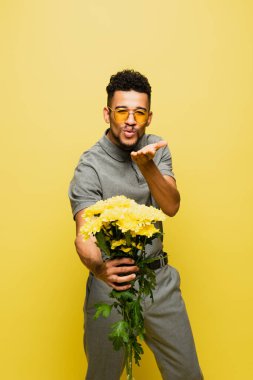 Güneş gözlüklü şık Afrikalı Amerikalı adam elinde bir buket çiçekle hava öpücüğü yolluyor. 
