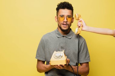 Şok olmuş, güneş gözlüklü, gri tenis tişörtlü, Afro-Amerikan bir adamın yanında cep telefonu tutan kadın. 