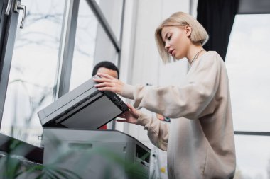 blonde woman using printer near african american manager  clipart