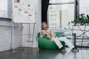 Sırıtan bir menajer koltukta oturuyor ve elinde akıllı telefon tutuyor. 