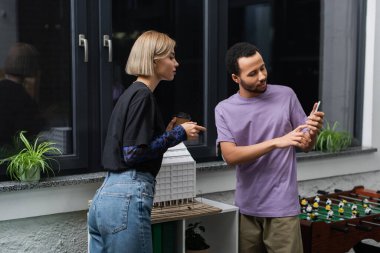 Afrikalı Amerikalı iş arkadaşının yanındaki akıllı telefonu işaret eden sarışın kadın. 