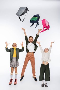 happy schoolboy and schoolgirls throwing backpacks on white  clipart