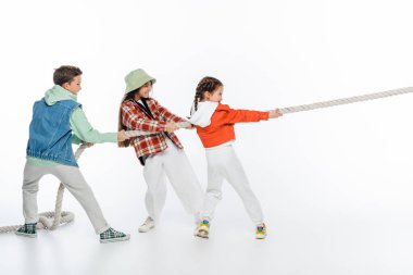 side view of happy preteen children pulling rope while playing tug of war game on white clipart