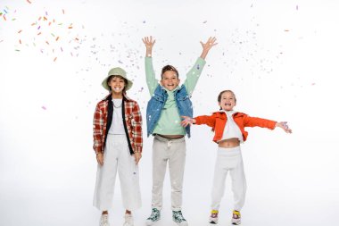 Elleri havada, kızların yanında duran ve beyaz konfetiye düşen pozitif çocukluk çağında bir erkek çocuğu.