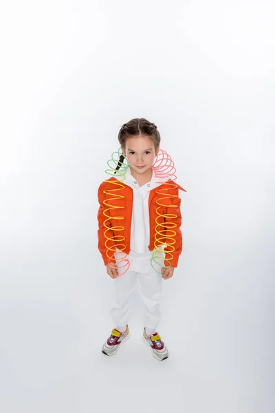 Plná Délka Usměvavé Dítě Oranžové Bundě Hrát Duhou Slinky Bílém — Stock fotografie