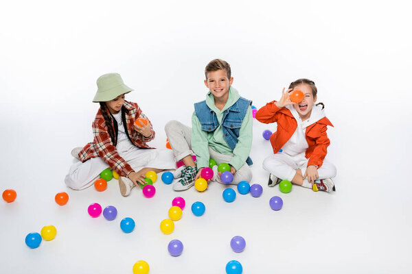 cheerful preteen kids sitting and playing with colorful balls on white 