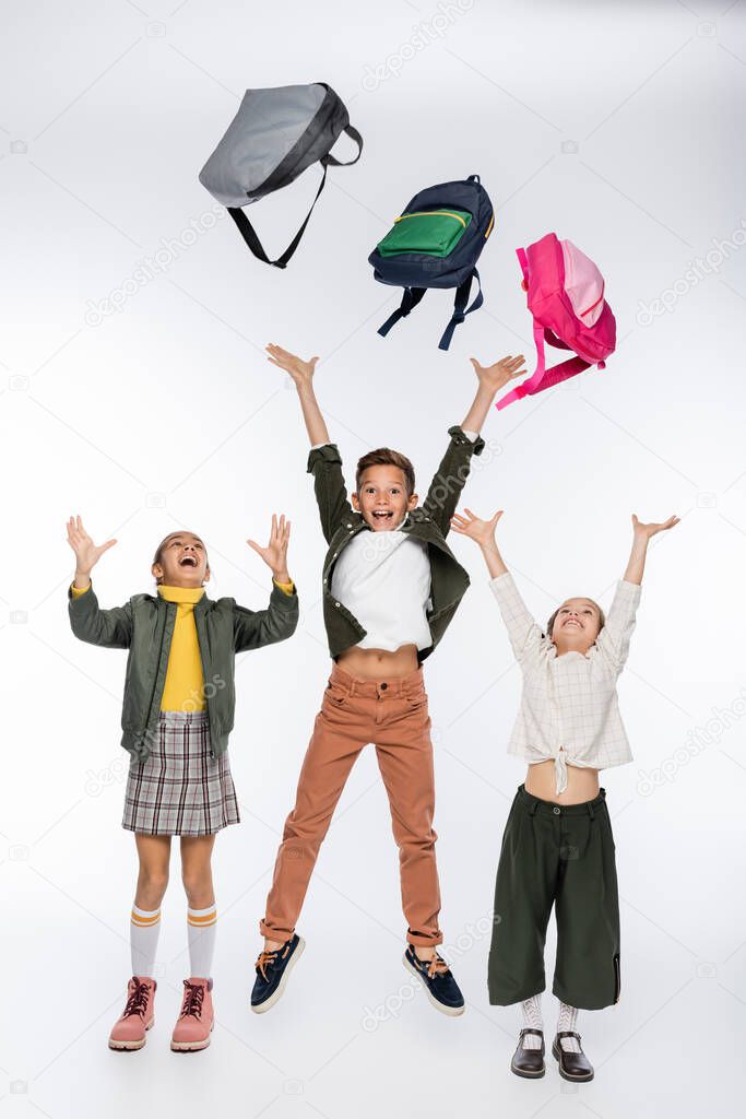 happy schoolboy and schoolgirls throwing backpacks on white 