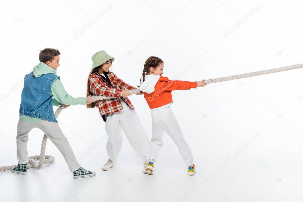 side view of happy preteen children pulling rope while playing tug of war game on white