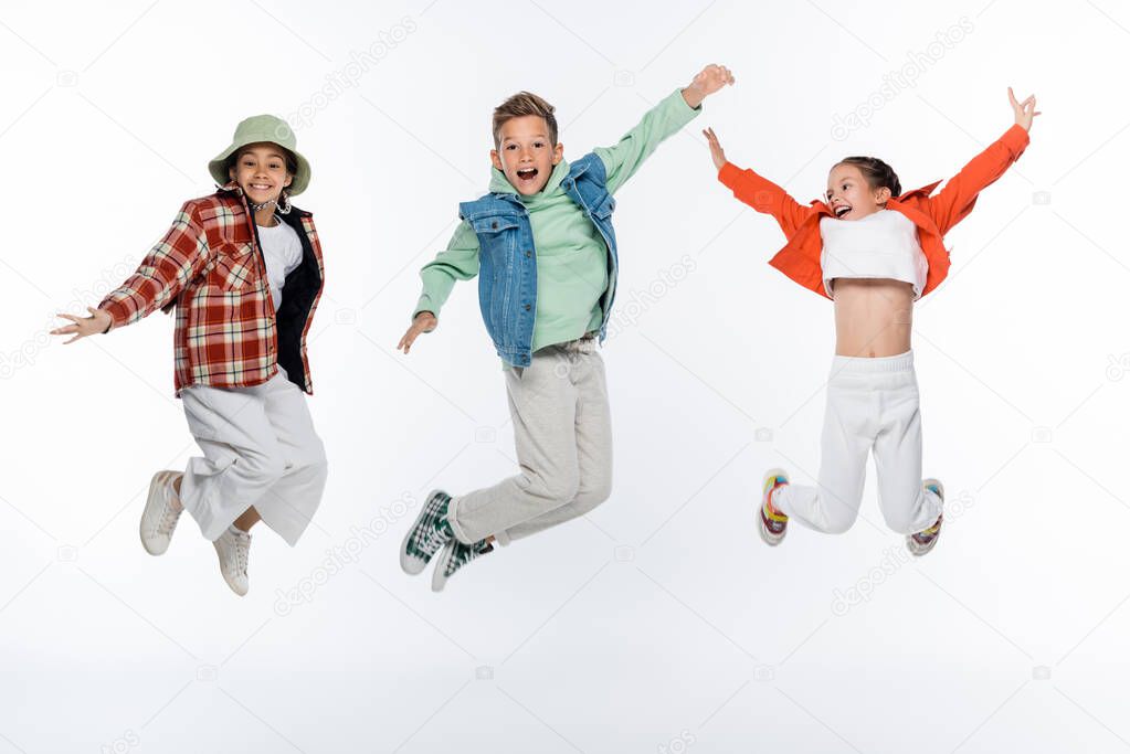 full length of stylish kids smiling while levitating on white
