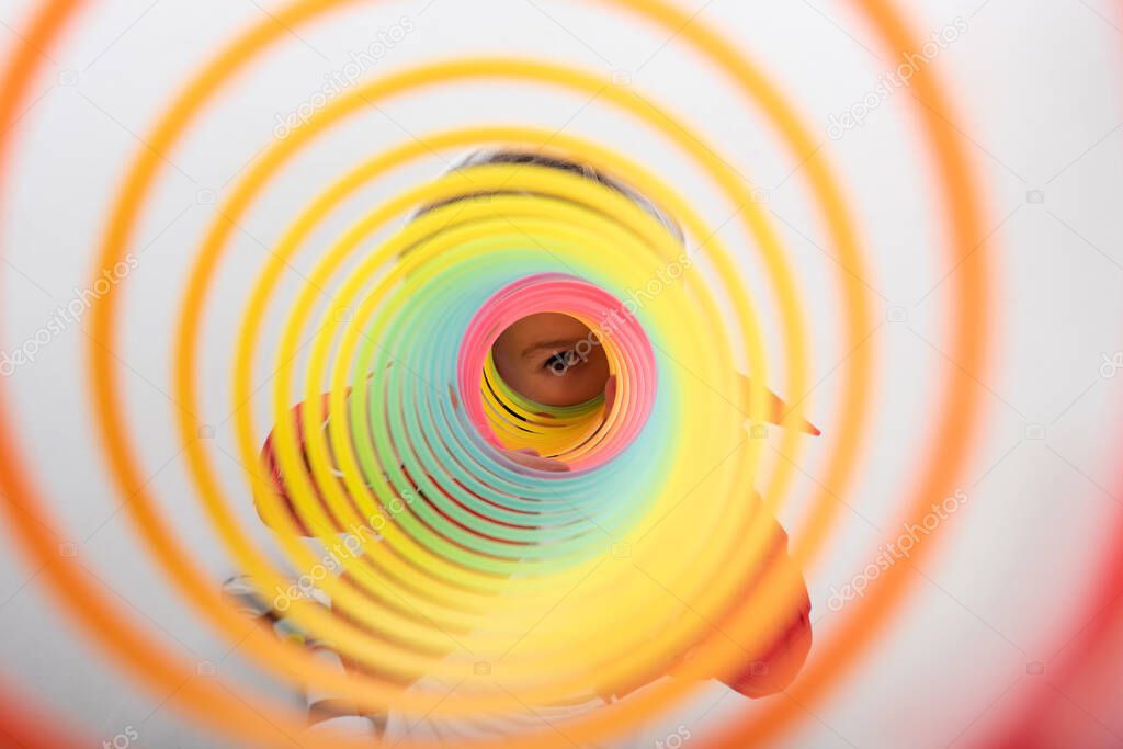 kid looking and camera through rainbow slinky on white