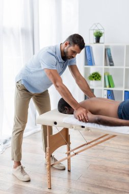 Genç fizyoterapist masaj masasındaki Afrikalı Amerikalı adama rehabilitasyon uyguluyor.