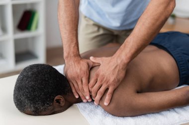 Fizyoterapist, olgun Afrikalı Amerikalı bir adama boyun ve omuz masajı yapıyor.