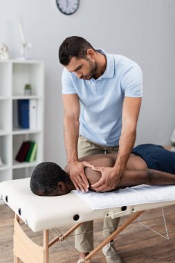 Orta yaşlı Afrikalı Amerikalı bir adamın omuzuna masaj yapan fizyoterapist.