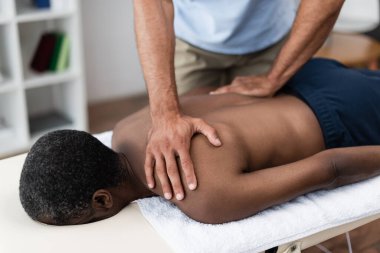 Afrikalı Amerikalı adam rehabilitasyon sırasında omuz masajı yaptırıyor.