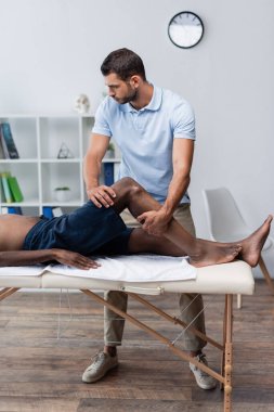 Rehabilitasyon uzmanı, masaj masasında yatan Afrikalı Amerikalıyı tedavi ediyor.