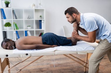Rehabilitasyon merkezinde masaj masasında yatan olgun Afro-Amerikalı bir adam.