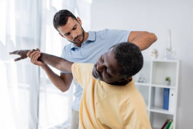 Genç doktor, rehabilitasyon merkezinde olgun bir Afrikalı Amerikalı hastayı muayene ediyor.