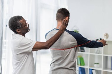 Afrikalı Amerikan rehabilitasyon eğitmeni direniş bandıyla çalışan bir adama yardım ediyor.