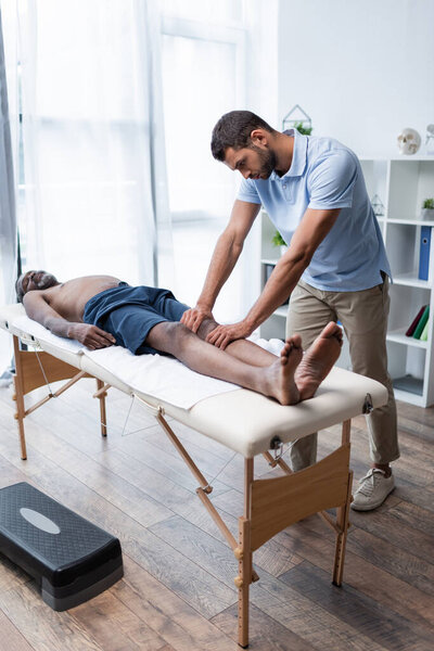 full length view of mature african american man lying on massage table during massotherapy 