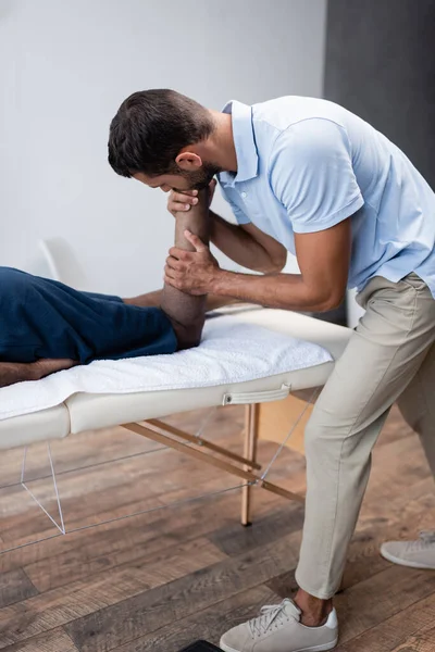 Fysiotherapeut Stretching Been Van Afrikaanse Amerikaanse Man Tijdens Revalidatie Procedure — Stockfoto