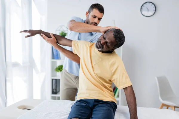 Rehabilitologist Stretching Arm Neck African American Man Clinic — Fotografia de Stock