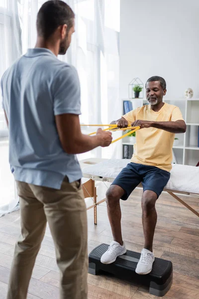 Uomo Afro Americano Che Esercizio Riabilitazione Con Elastici Fisioterapista Offuscato — Foto Stock
