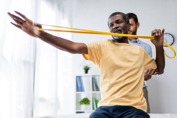 physical therapist assisting african american man working out with elastics