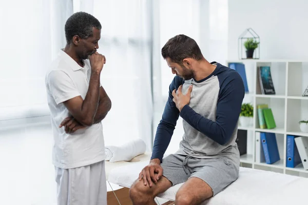 Mladý Muž Dotýká Hrudníku Blízkosti Přemýšlivý Africký Americký Lékař Rehabilitační — Stock fotografie