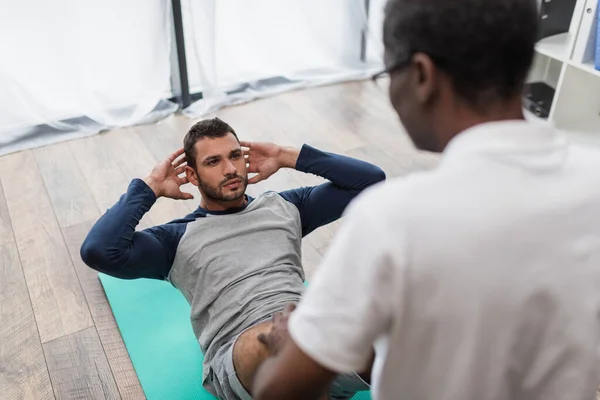 Wazig Afrikaans Amerikaans Fysiotherapeut Assisteren Man Doet Buikspieroefeningen Fitness Mat — Stockfoto