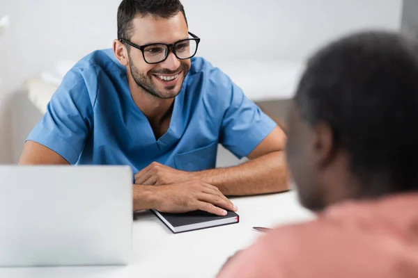 Young Doctor Eyeglasses Smiling Blurred African American Patient Consulting Room — Fotografia de Stock